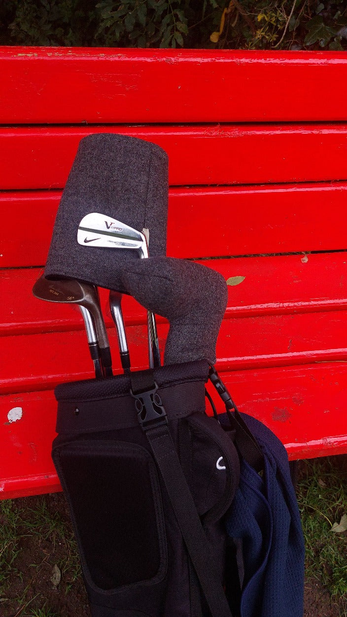 Golf bag and clubs, with charcoal headcovers, set against a re bench